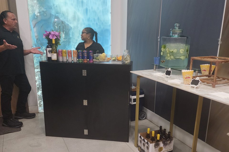 Black wooden folding mobile bar set up at an event, styled with bottles and glassware