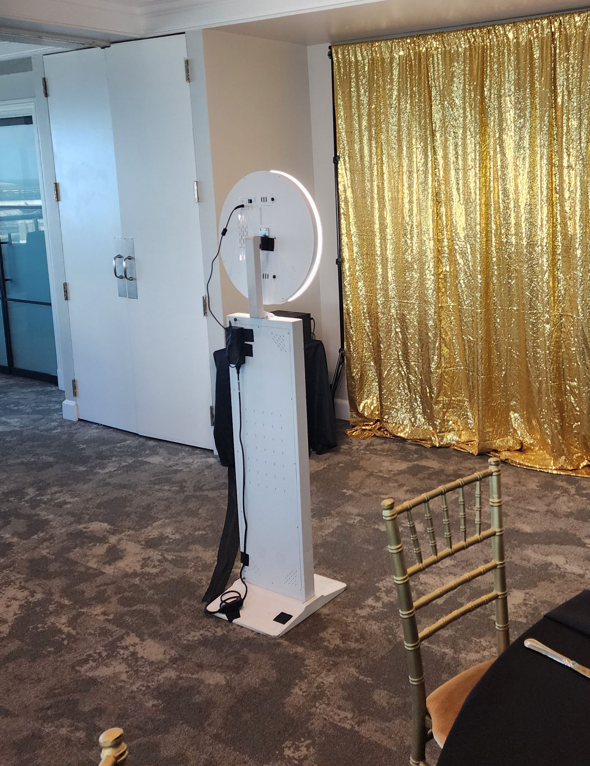 White selfie station kiosk with LED ring light at an event with gold chiavari chairs and a gold sequin backdrop